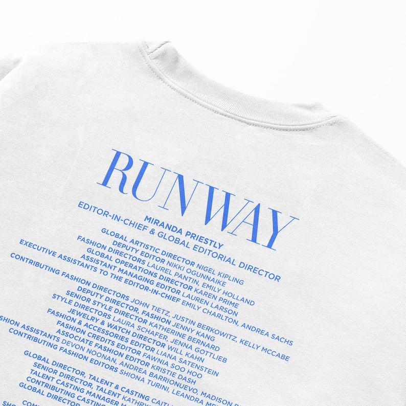Pode incluir: Uma camiseta branca com o texto "RUNWAY" em letras azuis. O texto "EDITOR-IN-CHIEF & GLOBAL EDITORIAL DIRECTOR" &eacute; impresso abaixo do logotipo, seguido de uma lista de nomes e t&iacute;tulos, incluindo Miranda Priestly, Nigel Kipling e John Tietz.