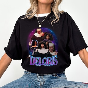 Peut inclure: T-shirt noir avec un graphisme coloré de Deloris Van Cartier du film Sister Act. Le design comprend plusieurs images du personnage avec le texte "Deloris Van Cartier" dans une police rétro. Le t-shirt est un vêtement décontracté.