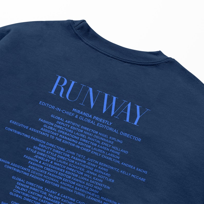 Pode incluir: Uma camiseta azul marinho com a palavra "RUNWAY" impressa em branco. A parte de tr&aacute;s da camiseta lista os nomes e os t&iacute;tulos da equipe editorial da revista.