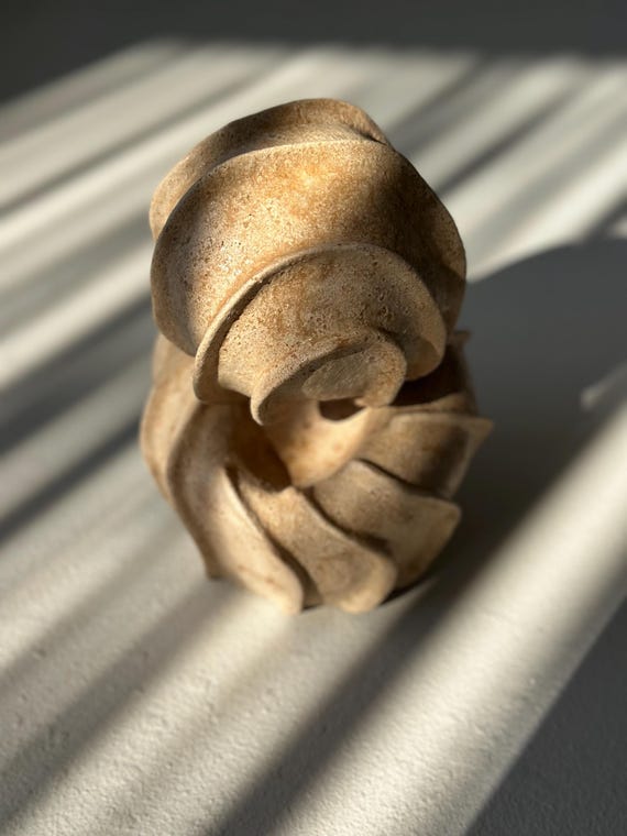 A hefty handmade stoneware ceramic sculpture in textured beige — the kind of abstract modernist object that anchors a shelf or coffee table and looks like it belongs in a gallery.