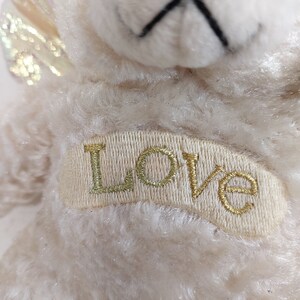 May include: A white plush teddy bear with a gold glitter wing and the word "LOVE" embroidered on its chest.