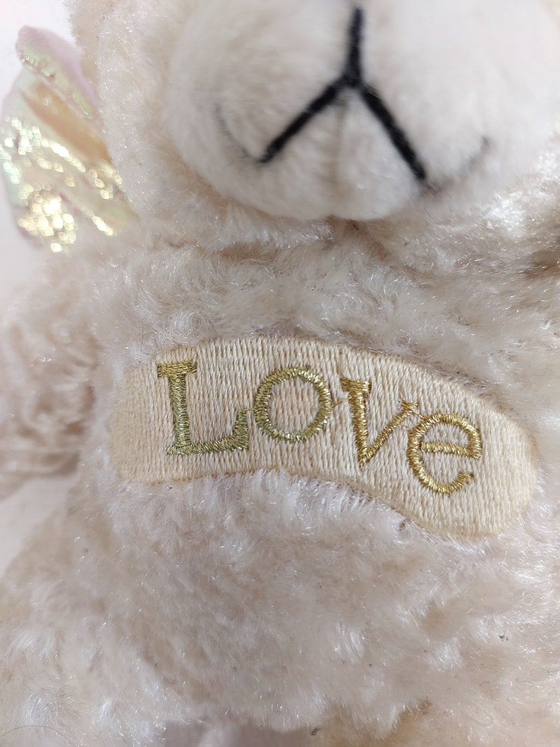 May include: A white plush teddy bear with a gold glitter wing and the word "LOVE" embroidered on its chest.