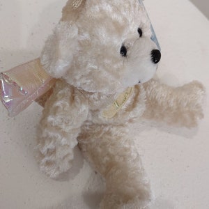 May include: A white plush teddy bear with iridescent wings. The bear is wearing a gold ribbon around its neck.