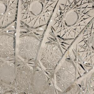 May include: A clear glass bowl with a cut glass design. The bowl has a scalloped edge and a starburst pattern.