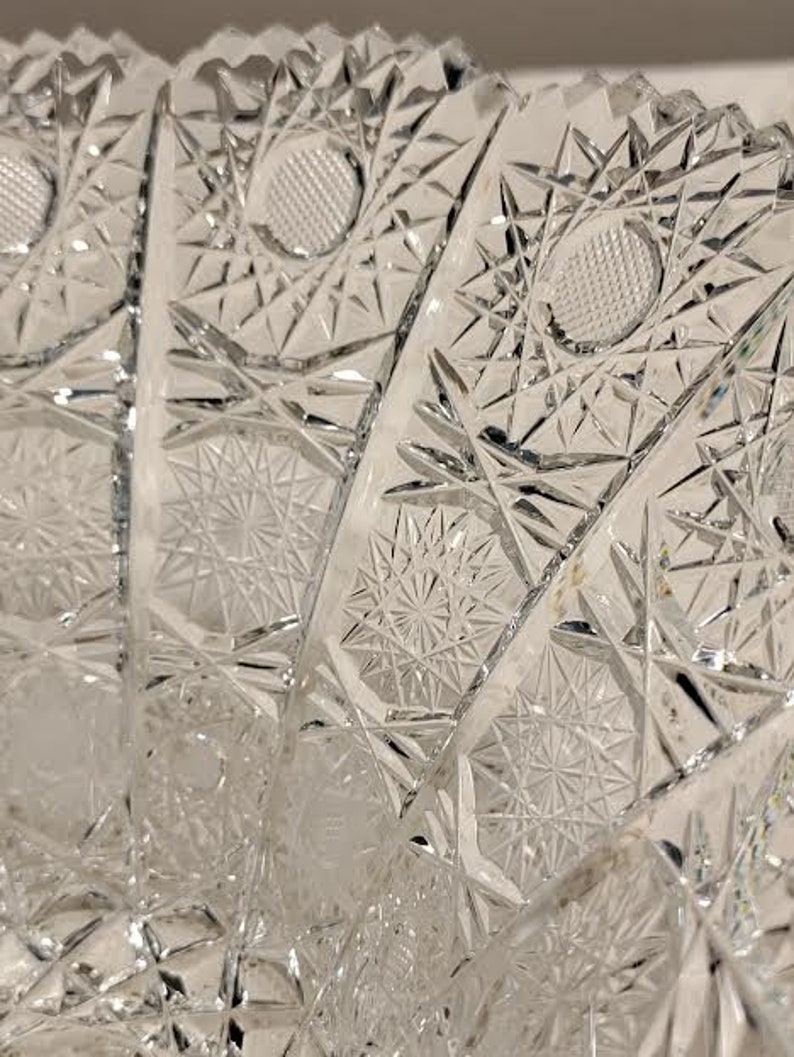 May include: A clear glass bowl with a cut glass design. The bowl has a scalloped edge and a starburst pattern.