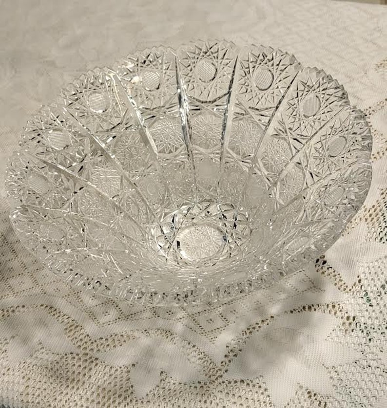 May include: A clear glass bowl with a cut glass design. The bowl has a scalloped edge and a wide, shallow base.