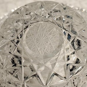 May include: A clear glass bowl with a geometric pattern. The bowl has a starburst design in the center.