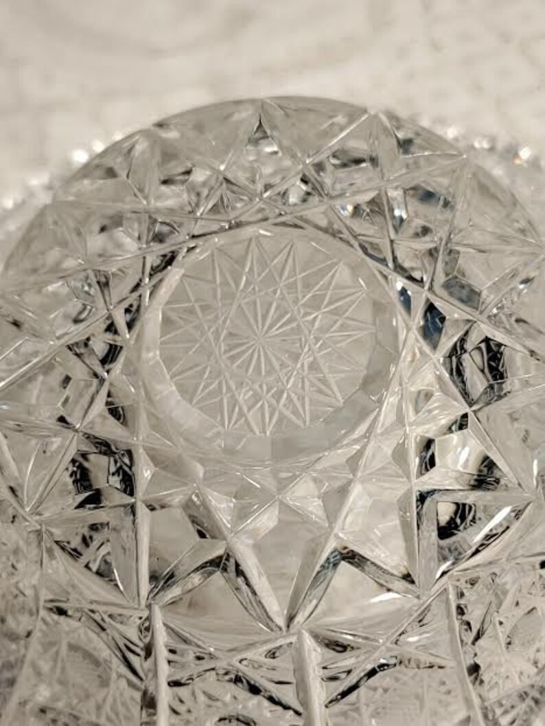 May include: A clear glass bowl with a geometric pattern. The bowl has a starburst design in the center.