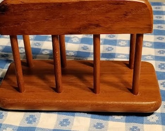May include: A wooden napkin holder with a natural finish. The holder has four vertical supports and a rectangular base.
