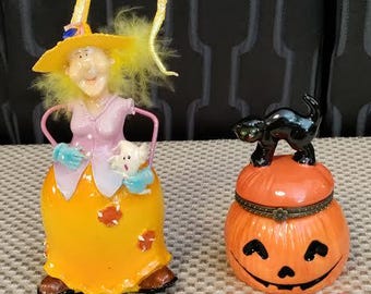 May include: A witch figurine with a yellow hat and dress, holding a small white cat. A pumpkin-shaped trinket box with a black cat on top.