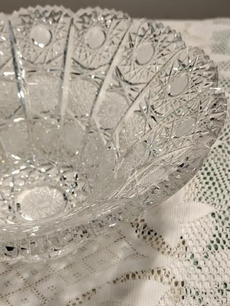 May include: A clear glass bowl with a cut glass design. The bowl has a scalloped edge and is made of crystal.