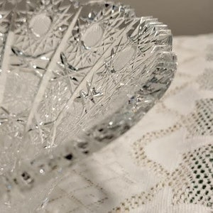May include: A clear glass bowl with a cut glass design. The bowl has a scalloped edge and a starburst pattern.
