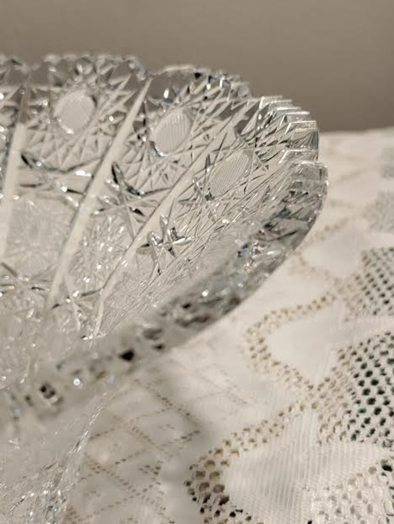 May include: A clear glass bowl with a cut glass design. The bowl has a scalloped edge and a starburst pattern.