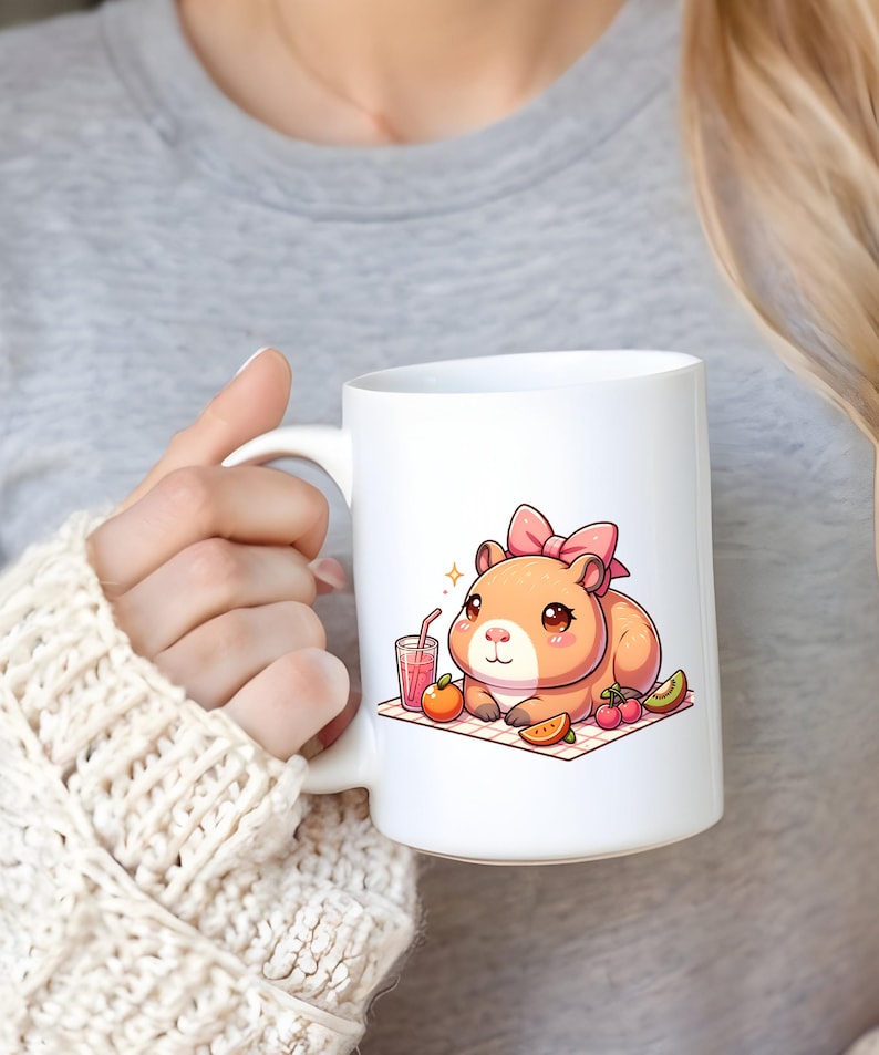 K&ouml;nnte beinhalten: Wei&szlig;e Keramiktasse mit einer Cartoon-Illustration eines Hamsters mit einer rosa Schleife, der ein Picknick mit Obst und Saft genie&szlig;t.