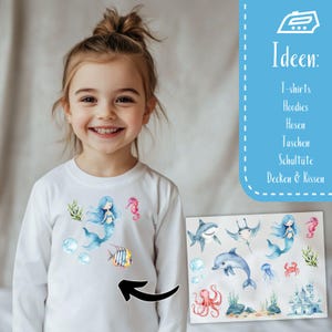 Peut inclure: Un t-shirt blanc &agrave; manches longues avec un motif color&eacute; de sir&egrave;ne et de cr&eacute;atures marines. Le motif comprend une sir&egrave;ne, un hippocampe, un poisson et des bulles. Des &eacute;l&eacute;ments de design suppl&eacute;mentaires sont affich&eacute;s.