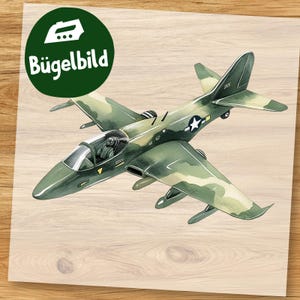 Peut inclure: Un écusson thermocollant représentant un avion de chasse militaire détaillé en camouflage vert et beige. L'avion a un emblème d'étoile blanche et est posé sur un fond clair en grain de bois. Un cercle vert avec le mot allemand "Bügelbild" est en haut à gauche.