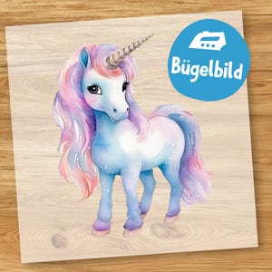 Pode incluir: Ilustração em aquarela de um unicórnio com chifre prateado, corpo azul e crina e cauda rosa e roxa esvoaçantes. A imagem tem um fundo azul claro com salpicos brancos. Um círculo azul com o texto "Bügelbild" está no canto superior direito.