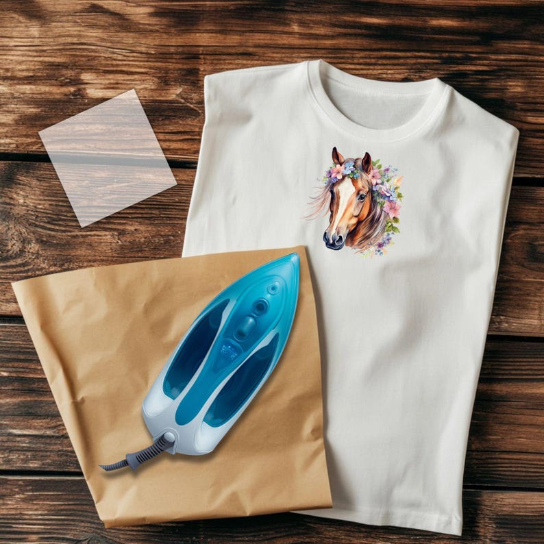 May include: White t-shirt featuring a watercolor horse head with a floral crown. A blue and white iron, a sheet of parchment paper, and a clear sheet are next to the shirt on a wooden surface. The horse design is in shades of brown, pink, and purple.