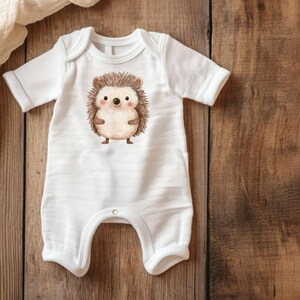 May include: White baby onesie featuring a brown and white hedgehog illustration. The hedgehog has a cute face with black eyes and a pink nose.