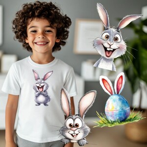 K&ouml;nnte beinhalten: Ein wei&szlig;es T-Shirt mit einem Cartoon-Bild eines grauen Kaninchens mit einem gro&szlig;en L&auml;cheln und offenem Mund. Es gibt drei weitere Bilder von Kaninchen mit gro&szlig;en L&auml;cheln und offenem Mund, eines davon mit einem blauen und gr&uuml;nen Osterei.