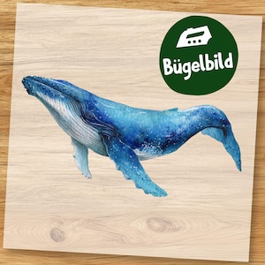 May include: A watercolour illustration of a blue whale with white detailing, set against a wood-grain background. The whale is shown swimming. A green circle with the text "Bügelbild" is in the upper right corner.