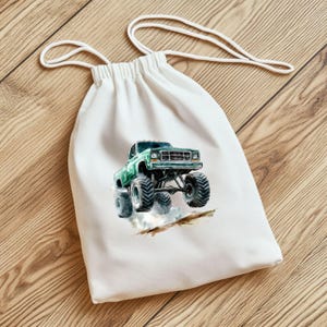 Puede incluir: Una bolsa de tela blanca con un gr&aacute;fico de cami&oacute;n monstruo verde impreso en la parte delantera. El cami&oacute;n est&aacute; conduciendo por un camino de tierra y levantando polvo.