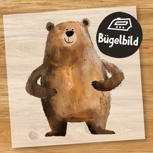 Könnte beinhalten: Ein brauner Bär mit freundlichem Gesichtsausdruck, der auf einem hellen Holzgrund steht. Das Bild ist mit "Bügelbild" beschriftet.