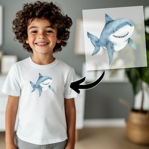 May include: A white t-shirt with a blue and gray watercolor shark graphic. The shark is smiling and has a white belly.