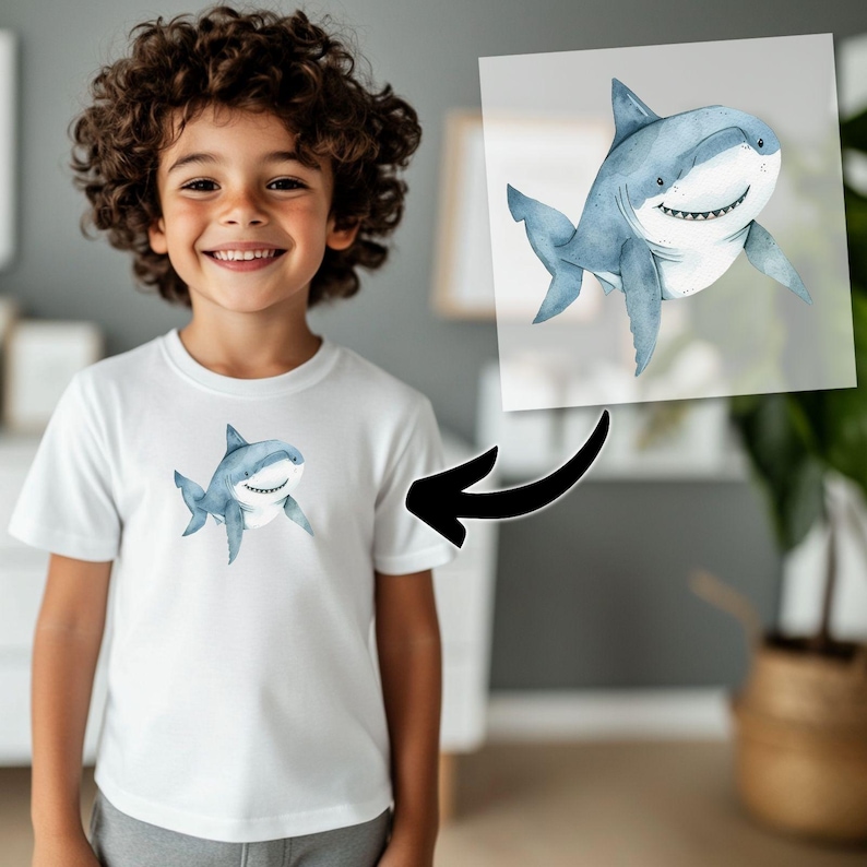 May include: A white t-shirt with a blue and gray watercolor shark graphic. The shark is smiling and has a white belly.