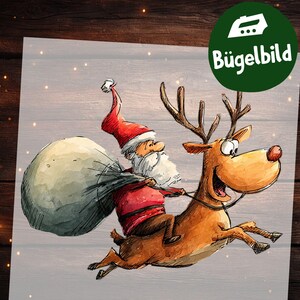 Op de afbeelding: Een feestelijke illustratie van de Kerstman op een rendier, met een zak vol cadeaus. De Kerstman draagt een rood pak en hoed. Het rendier is bruin met geweien en een rode neus. Met de tekst "Bügelbild".