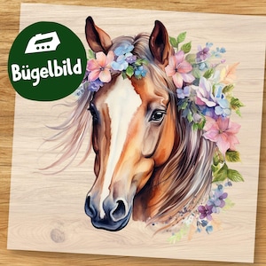 Könnte beinhalten: Aquarell-Illustration eines Pferdekopfes, geschmückt mit einem Blumenkranz. Das Pferd hat ein braunes Fell mit einer weißen Blesse und fließender Mähne. Der Blumenkranz zeigt rosa, blaue und violette Blumen. Der Text "Bügelbild" ist enthalten.