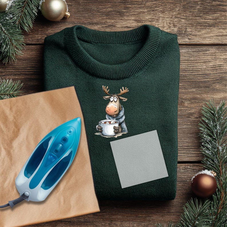 May include: A dark green sweater with a cartoon moose design holding a mug of hot chocolate. A blue and white iron and a gray patch are next to the sweater on a wooden surface. Christmas decorations are in the background.