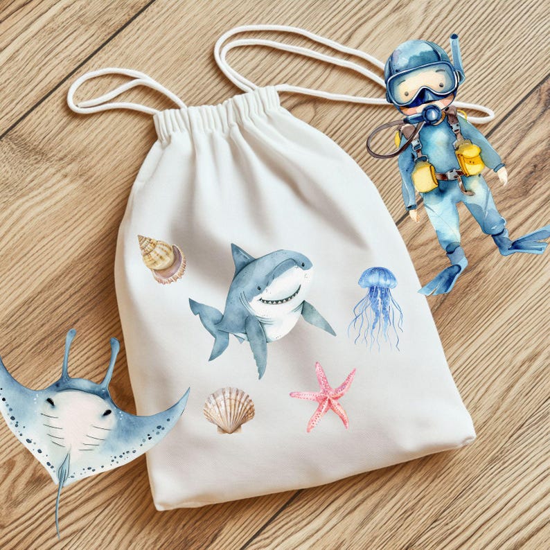 Peut inclure: Un sac blanc &agrave; cordon de serrage avec des illustrations &agrave; l'aquarelle d'un requin, d'une raie manta, d'une &eacute;toile de mer, d'une m&eacute;duse et de coquillages. Une illustration de plongeur est &eacute;galement pr&eacute;sente. Le sac est en tissu doux.