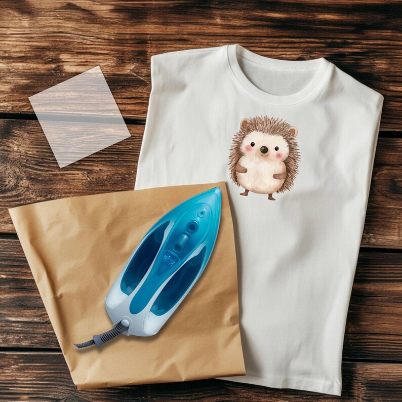 May include: A white t-shirt featuring a brown and white hedgehog illustration. A blue iron and brown paper are on a wooden surface.