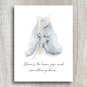May include: A watercolor illustration of a bride in a light blue wedding dress holding a bouquet of white and blue flowers. The text "Here's to love, joy, and something blue." is written below the bride.