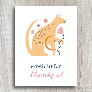 Illustrated greeting card featuring a stylized tan dog holding a pink flower, surrounded by pink flowers. Text below reads "Pawsitively Thankful" in playful navy and pink fonts.
