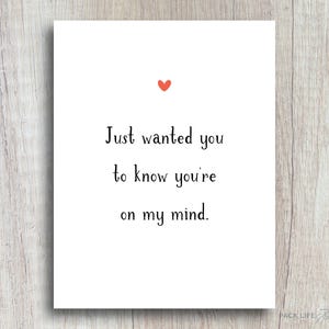 May include: A white rectangular greeting card featuring a small red heart icon centered at the top. Below the heart, the black text reads: Just wanted you to know you're on my mind. The card has a clean, simple design with black lettering on a white background.