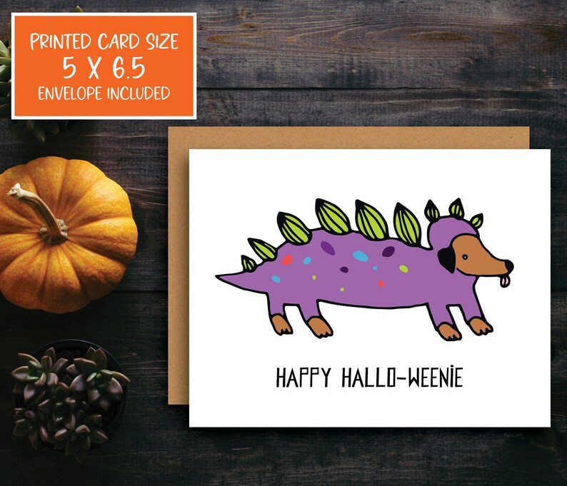 A cute and funny illustration of a dachshund dog wearing a dinosaur costume with the words happy halloweenie. Perfect greeting card for halloween and dog lovers.