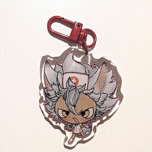 May include: A clear acrylic keychain with a cartoon character. The character has spiky white hair, a nurse's cap with a red cross, and an angry expression. It is holding a lollipop. The keychain has a red metal clasp.