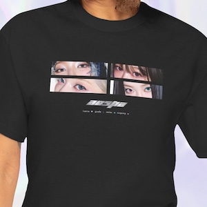 以下が含まれることがあります： 4つの目のグラフィックと銀色の文字で「aespa」と書かれた黒いTシャツ。グラフィックの下のテキストは「Love & Girls - Next Level - Girls - Savage」です。