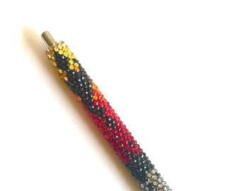 May include: A black, red, yellow, and silver pen covered in rhinestones.