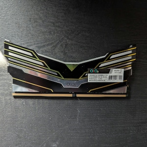 May include: A black and gold OLOy DDR4 RAM module. The module has a distinctive design with angular accents and the OLOy logo. The product information label is visible on the side. The RAM is designed for PC use.