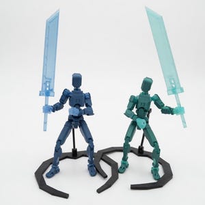 May include: Two articulated action figures, one navy blue and one teal, each holding a translucent blue sword. They stand on black, curved bases against a white background. The figures are posed as if in combat.