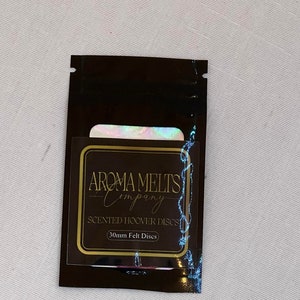 Puede incluir: Una bolsa marrón con una etiqueta dorada que dice "Aroma Melts Company" y "Scented Hoover Discs 30mm Felt Discs".