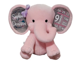Puede incluir: Elefante de peluche rosa con orejas grises. Las orejas tienen una inscripción blanca que dice "Sophia Denise" en una oreja y "06-29-23 9 libras 1 onza 20,0 pulgadas 02 17 am" en la otra oreja.