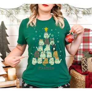 May include: Green t-shirt with a Christmas tree design featuring a stack of cats wearing Christmas lights. The text "Cute Christmas" is printed below the tree.