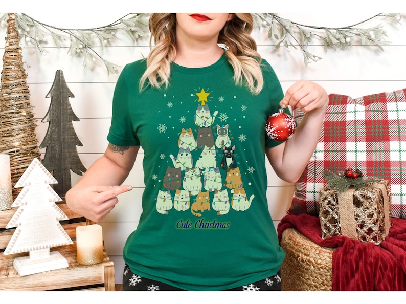 May include: Green t-shirt with a Christmas tree design featuring a stack of cats wearing Christmas lights. The text "Cute Christmas" is printed below the tree.