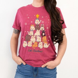 May include: A pink t-shirt with a Christmas tree design featuring a group of cats wearing Christmas lights. The text "Cute Christmas" is printed below the tree.