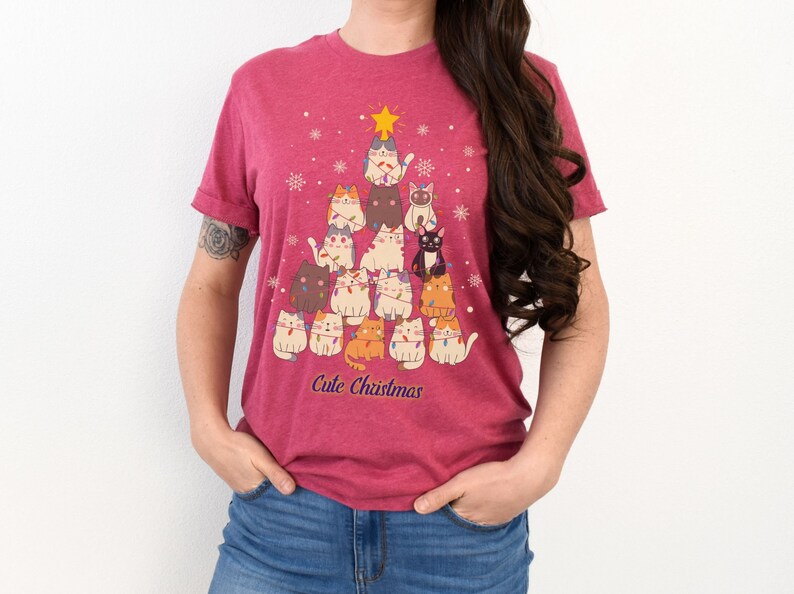 May include: A pink t-shirt with a Christmas tree design featuring a group of cats wearing Christmas lights. The text "Cute Christmas" is printed below the tree.