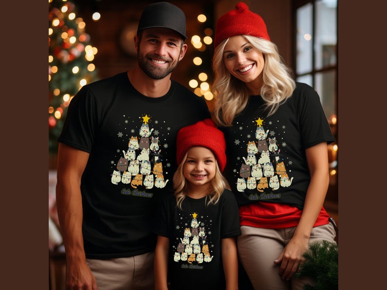 May include: A family of three wearing matching black t-shirts with a Christmas tree design featuring cats. The tree is decorated with a star and ornaments. The text "Kit's Christmas" is printed on the shirts.